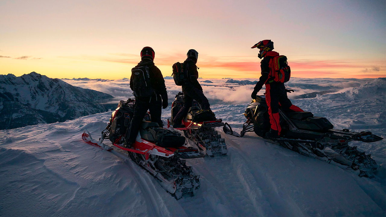 Three riders on a mountain with Lynx Snowmobiles when sun is going down