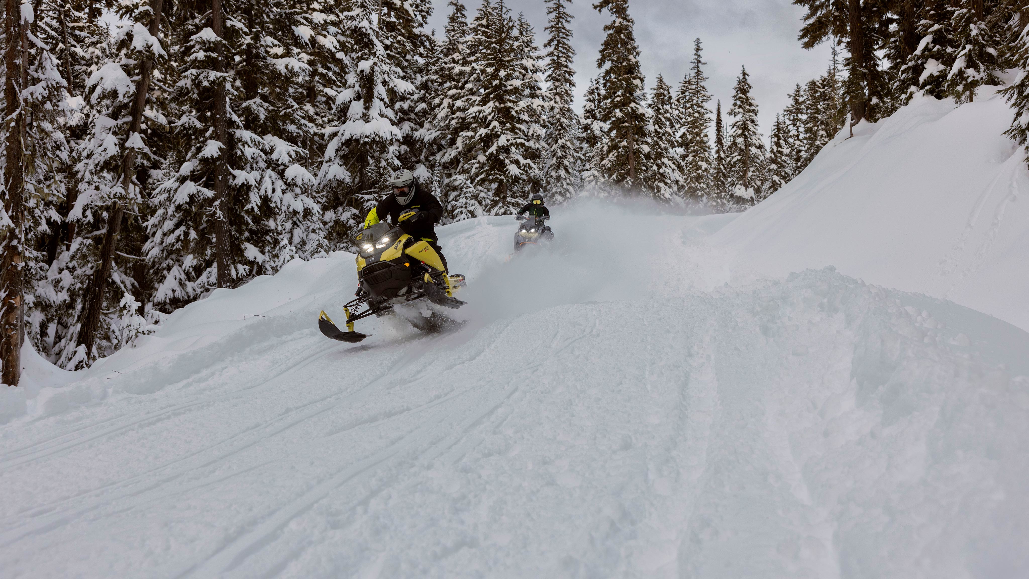 Dva skútre 2025 Ski-Doo Crossover jazdia vo vysokej rýchlosti lesom