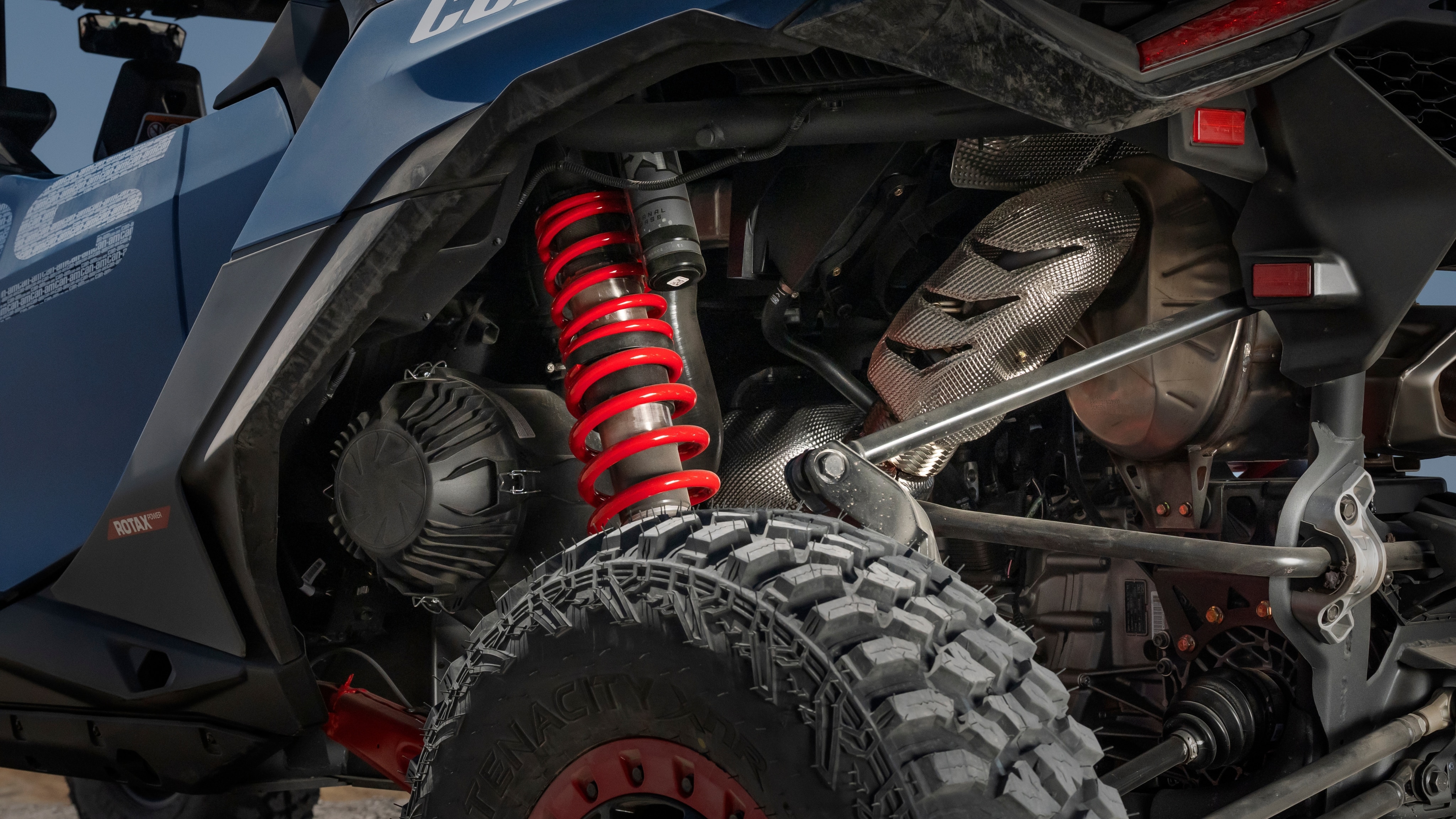 A close-up of the back and shock absorbers of a Can-Am Maverick R parked in a desert