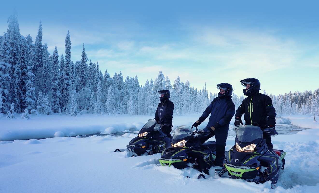 3 men are watching the view of the snow-covered forest, they each have a Lynx Xterrain Snowmobile Model