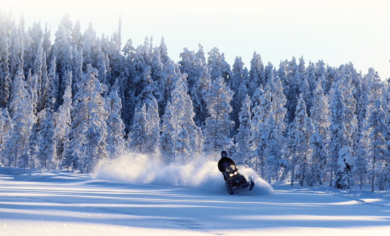 A man drifts in the snow with his Lynx Xterrain Snowmobile Model in the middle of the snowy forest