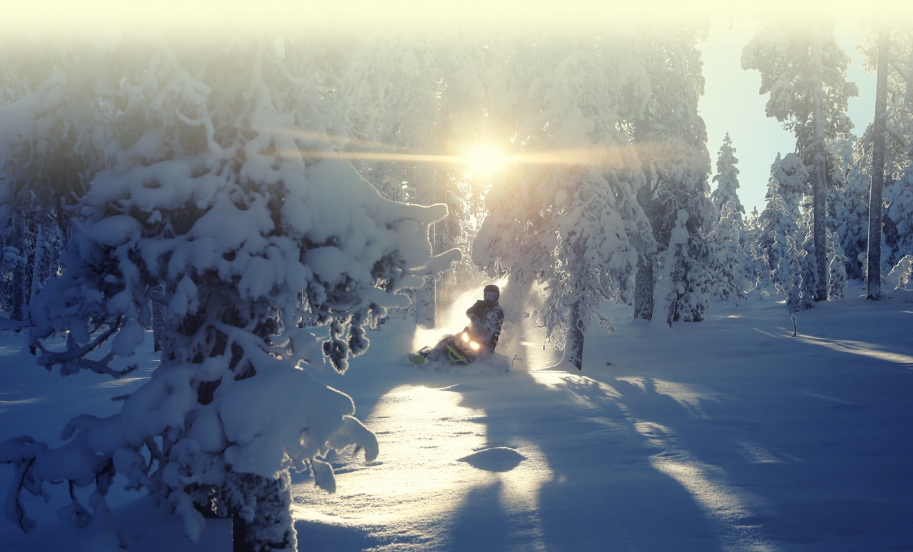Moški se s svojim modelom motornih sani Lynx Xterrain ob sončnem zahodu zanese v sneg