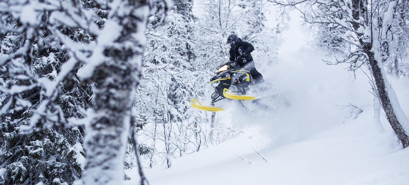 A man is jumping with his Lynx Xtrim Snowmobile Model in the snowy forest