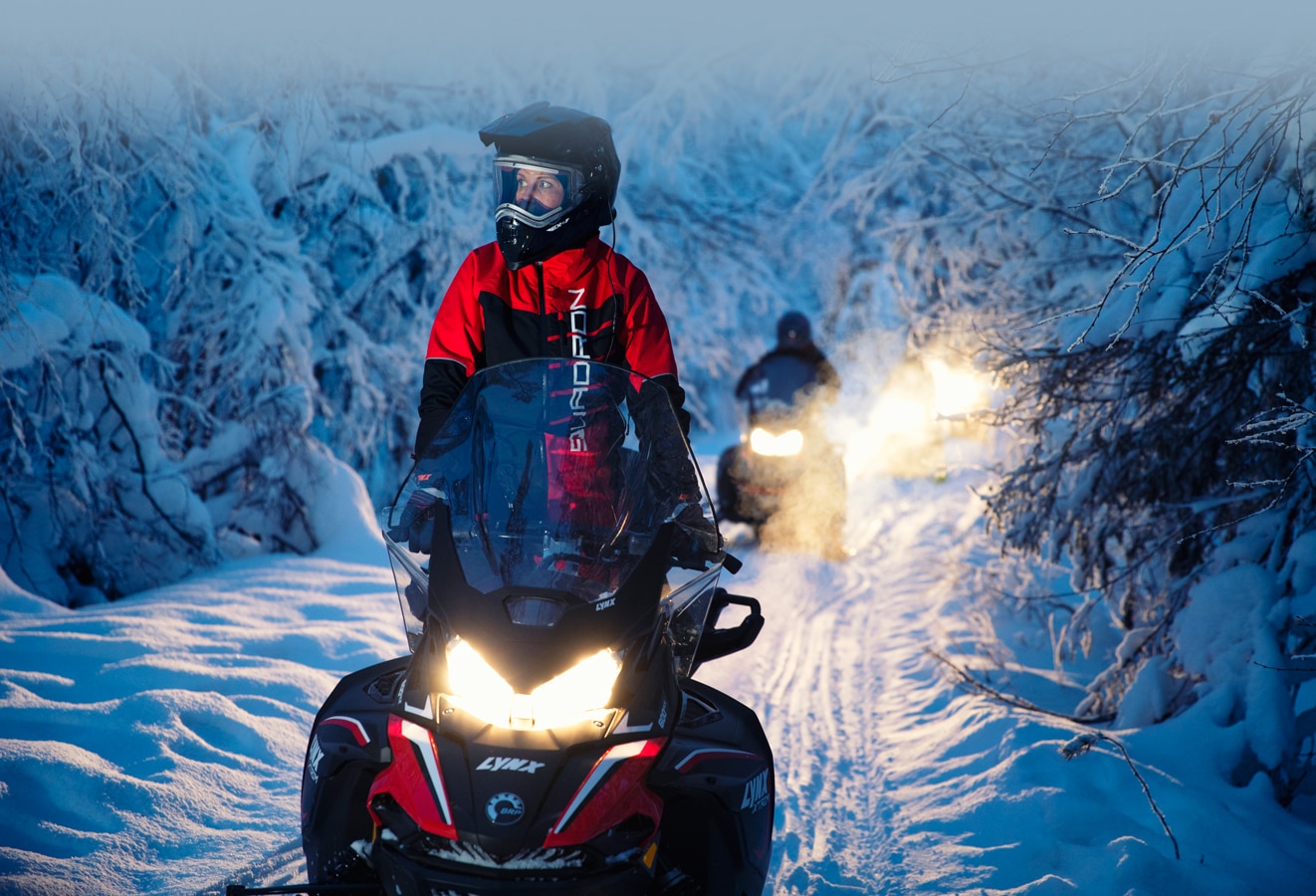 A group of drivers follow a snowy path in the forest with their Lynx Xtrim Snowmobile Model