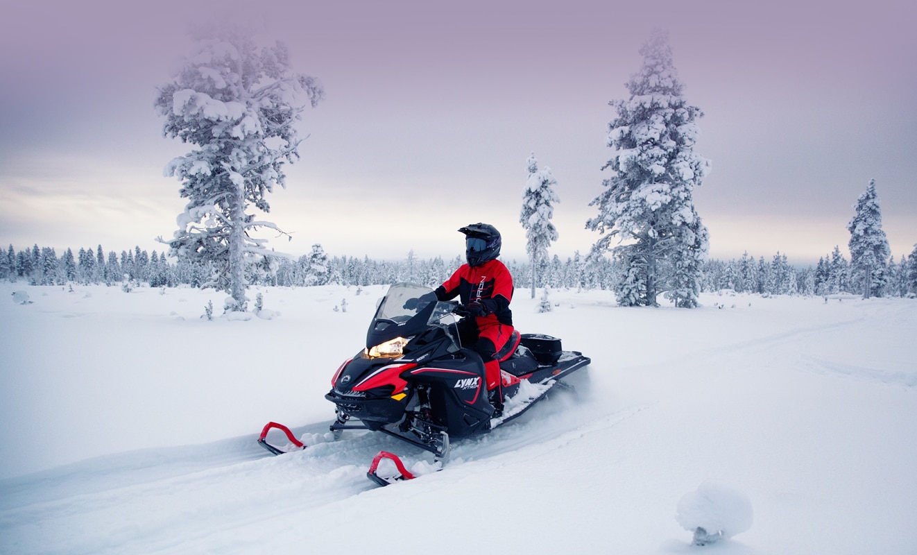 A man is riding his Lynx Xtrim Snowmobile Model on a snowy road