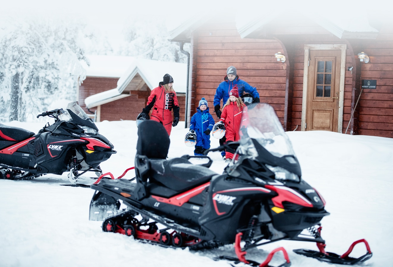 A family of 4 people are heading towards their 2 Lynx Xtrim Model Snowmobile 
