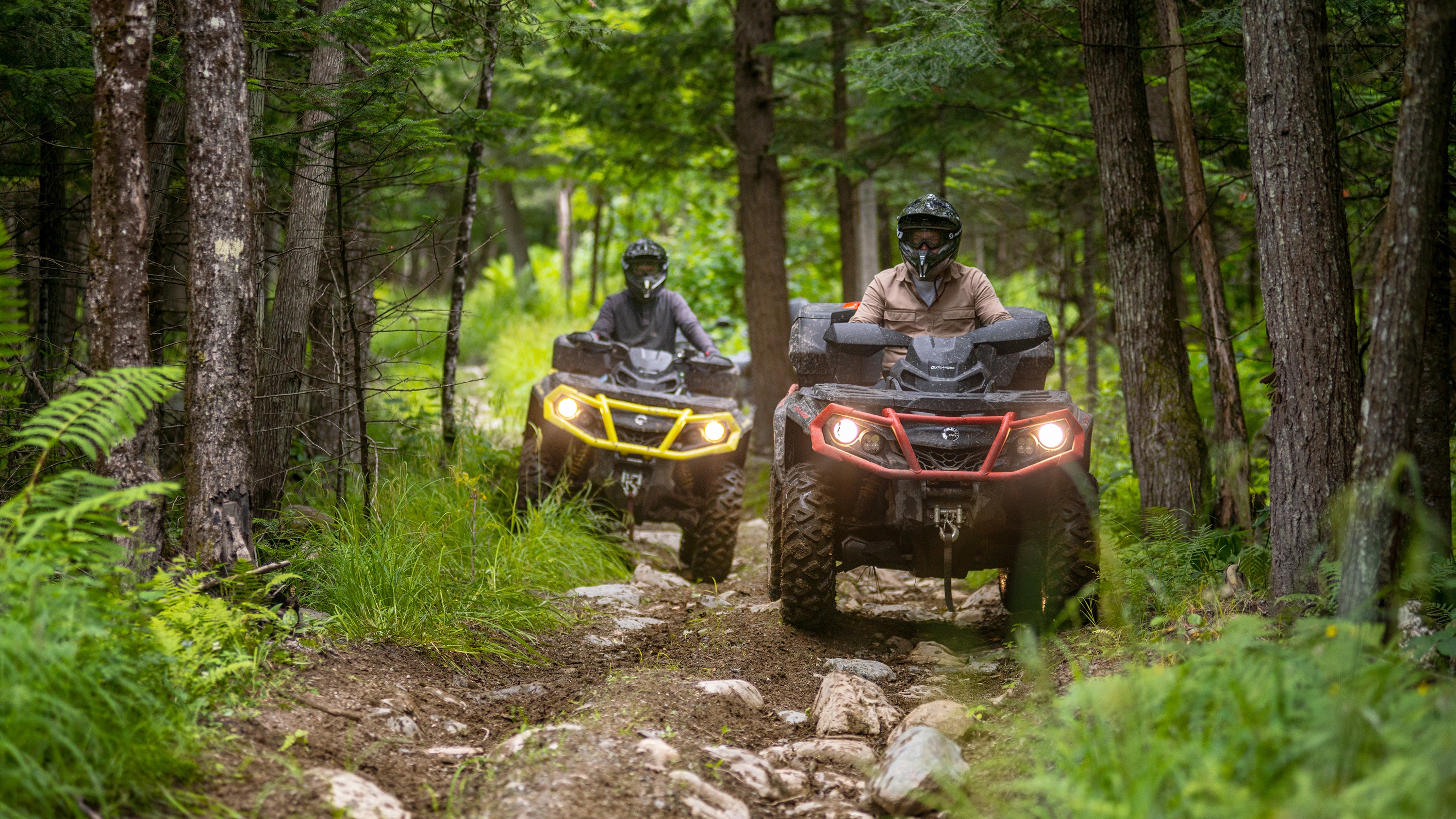 Two men driving their Outlander ATV through a forest trail