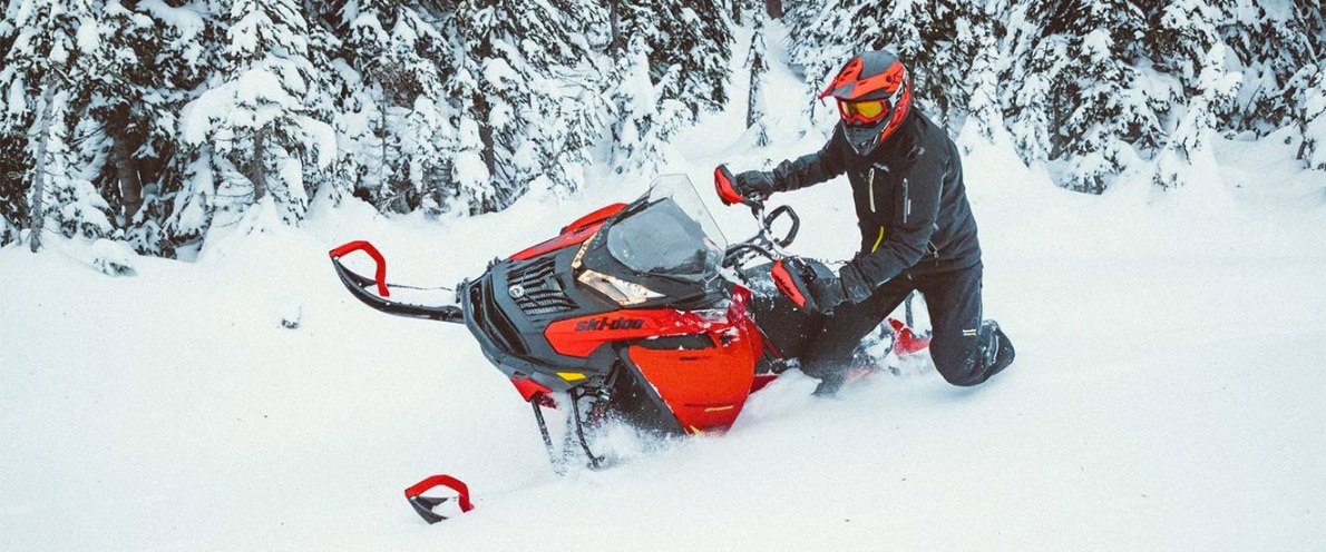 Čovjek koji pluta sa svojim motornim sanjkama Expedition klečeći na snijegu