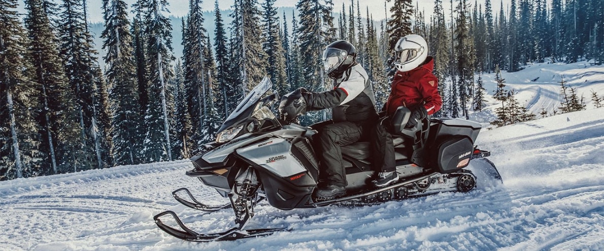 Burrë dhe grua duke vozitur nëpër dëborë në një Ski-Doo Grand Touring