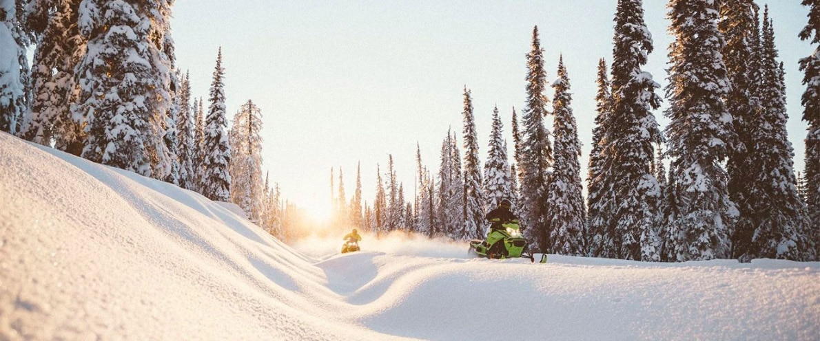  Dy burra që ngasin një Ski-Doo Renegade nëpër një shteg me dëborë