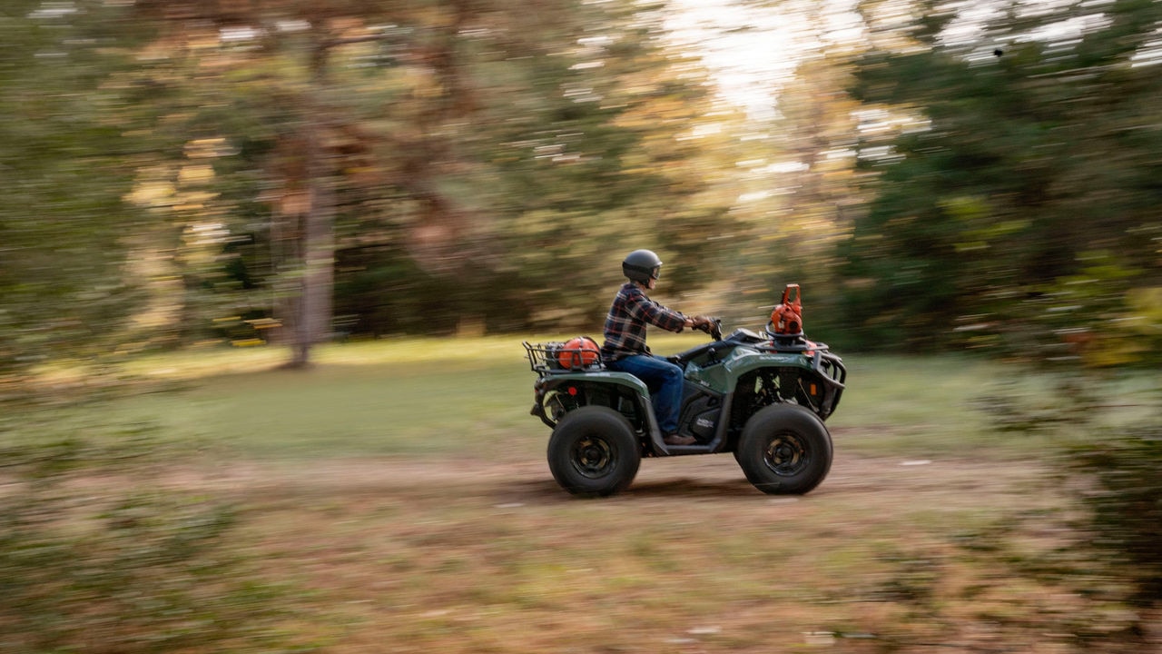 A rider on his Tundra Green Outlander PRO XU loaded with working gear, including the LinQ Chainsaw Holder