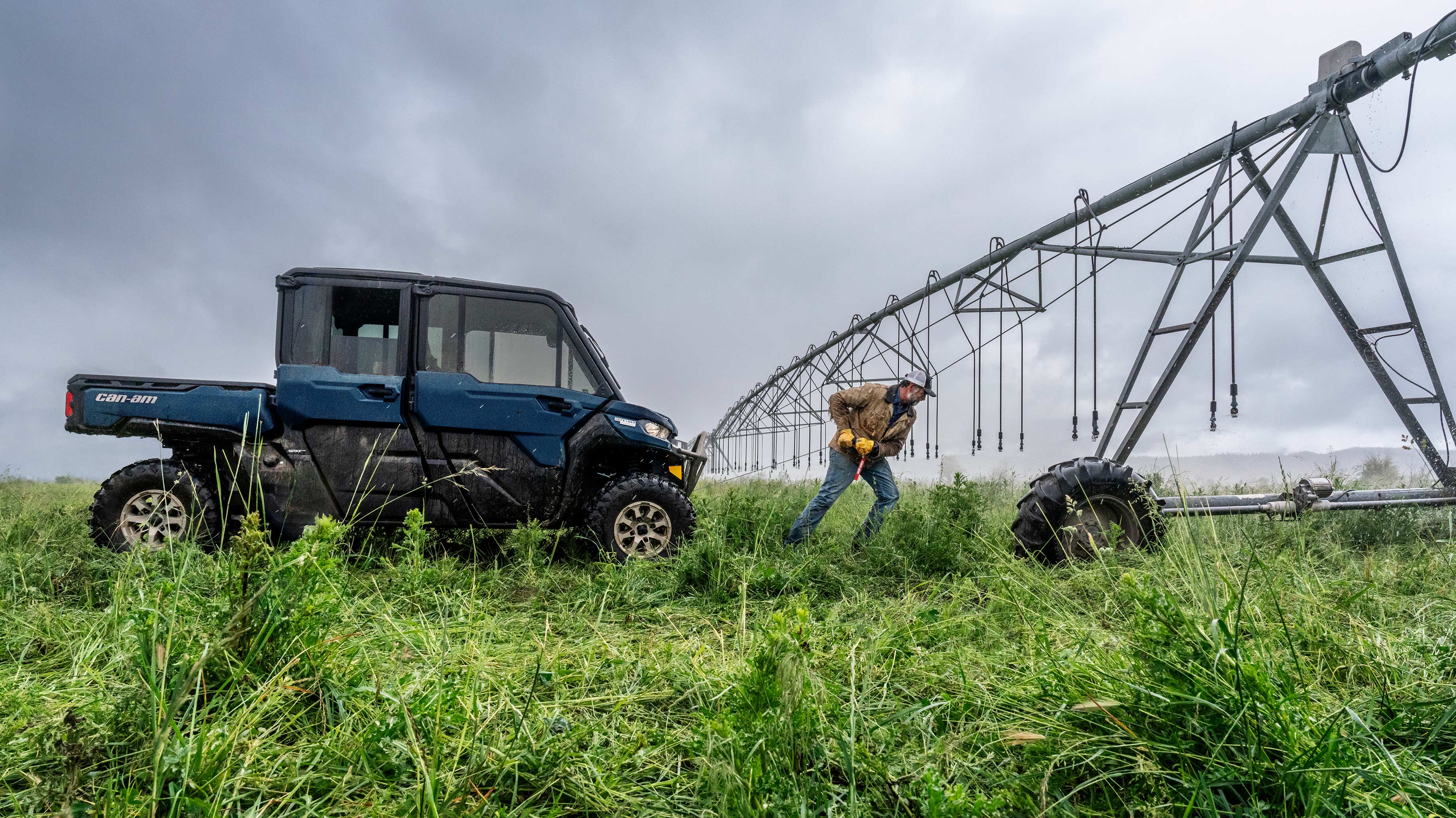 A farmer standing next to his Tundra Green Outlander PRO XU farm ATV in front of several stacked round hay bales