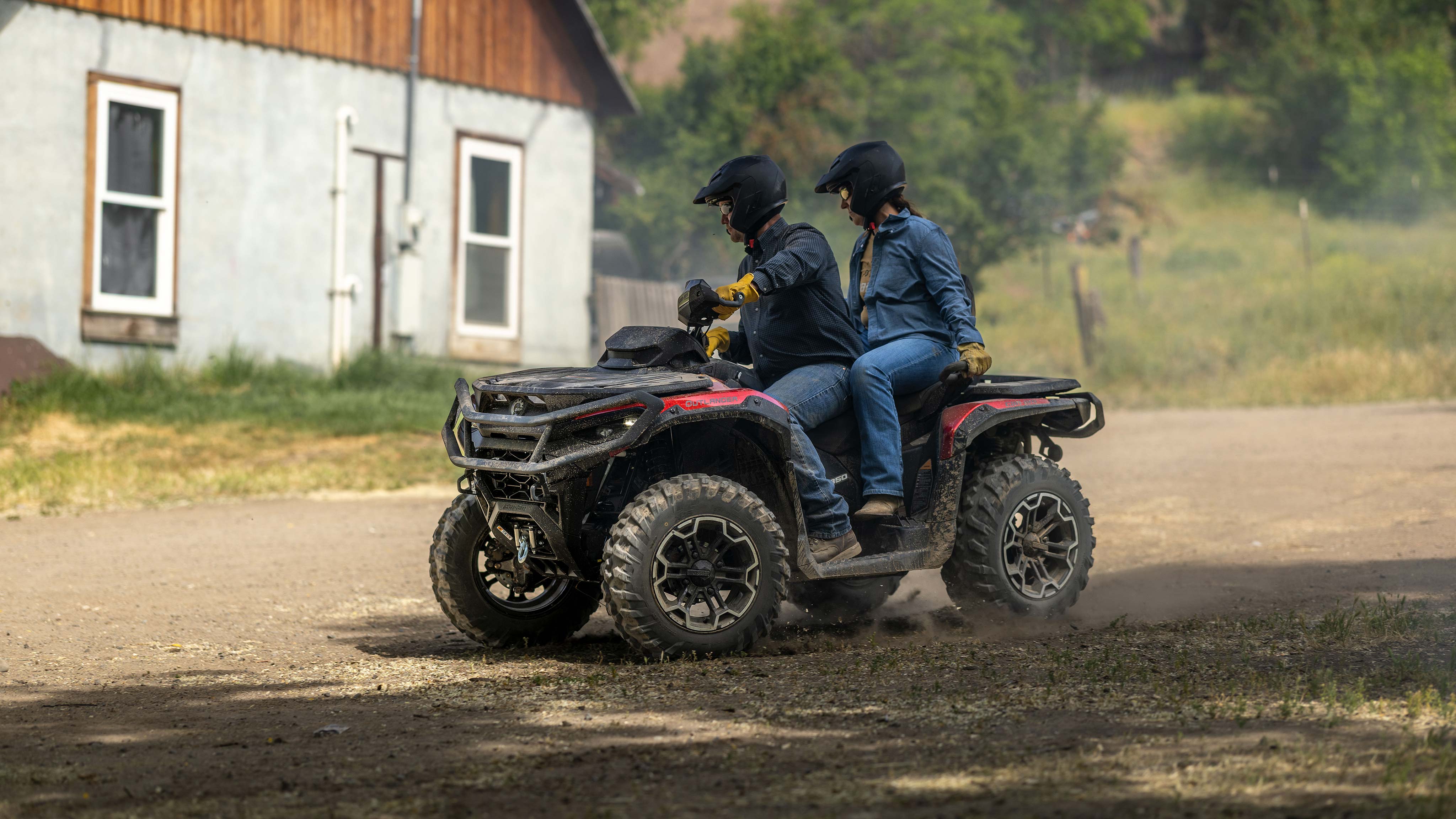 A man and a woman on a Can-Am Outlander Max XT 2025 on an unpaved road