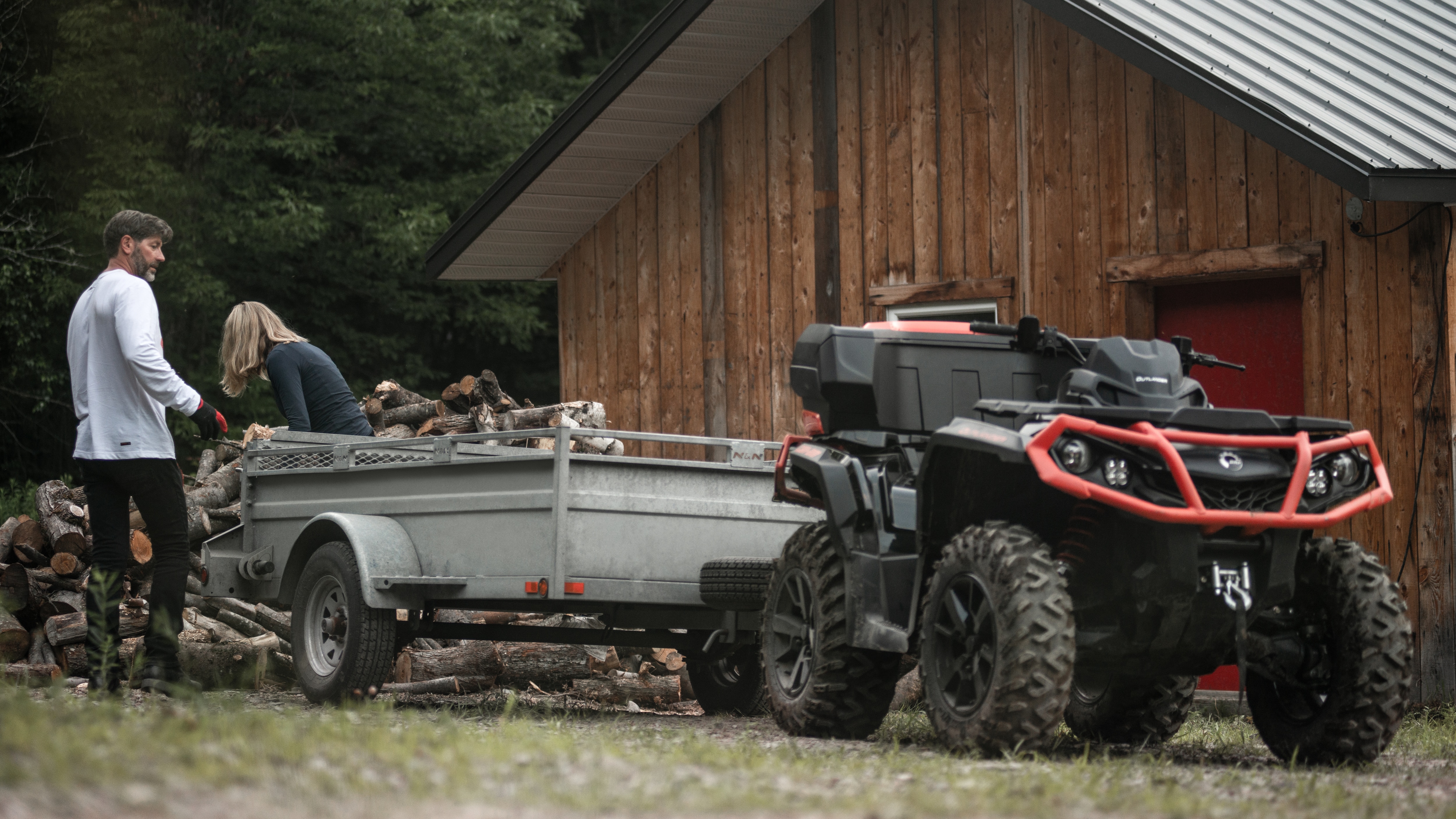 Dwie osoby ładujące drewno do przyczepy pojazdu Can-Am Outlander XT ATV